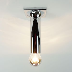 Może przedstawiać: Chromowana lampa sufitowa. Posiada kwadratową podstawę, cylindryczny korpus i kulistą żarówkę. Żarówka jest zapalona, emitując ciepłe światło.