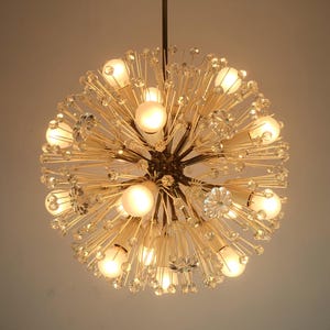 Op de afbeelding: Een ronde, bolvormige kroonluchter in goudkleur. De kroonluchter heeft veel kristal-achtige accenten en meerdere gloeilampen.