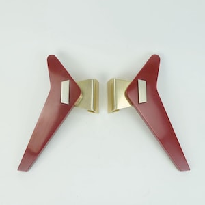 Può includere: Due gambe per mobili in stile mid-century. Ogni gamba è di un colore rosso-marrone scuro con un accento argentato e staffe in metallo dorato. Le gambe angolate hanno un design elegante e minimalista, adatto a vari mobili. Ogni gamba misura circa 20 cm.