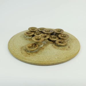 Puede incluir: Un plato de cerámica con un esmalte marrón claro y un grupo de pequeños candelabros de cerámica en forma de flor marrones.