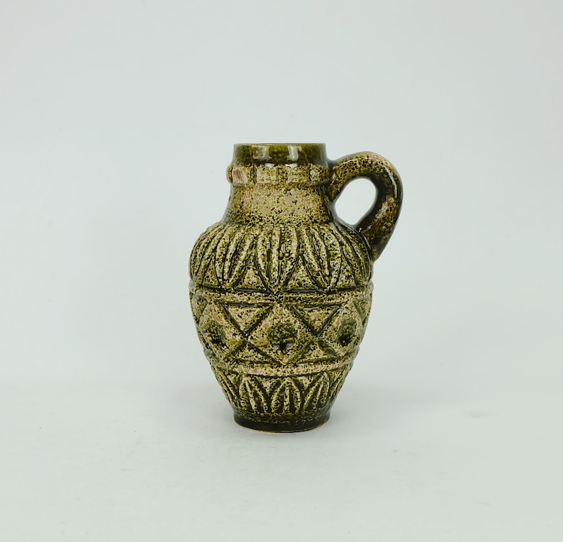 May include: A small green ceramic vase with a geometric pattern and a handle. The vase has a textured surface and a light brown color.