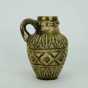 May include: A green ceramic vase with a textured, geometric design. The vase has a wide base and a narrow neck with a handle.