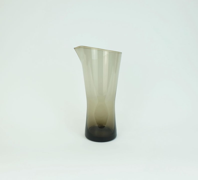 May include: A clear glass pitcher with a brown tint. The pitcher has a wide base and a narrow neck.