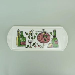 May include: A rectangular white serving tray with a decorative illustration of wine bottles, a glass, a lantern, and cherries. The tray has a ribbed edge design and is set against a light green background.