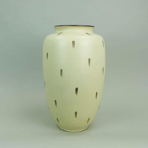 May include: Cream-colored ceramic vase with a rounded shape and a dark brown rim. The vase is decorated with vertical dark brown dashes scattered across the surface. A decorative piece for the home.