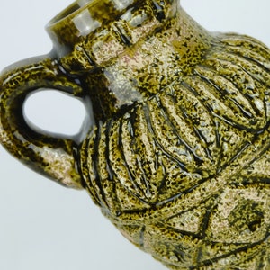 May include: A green ceramic vase with a textured surface and a geometric design. The vase has a wide mouth and a handle.