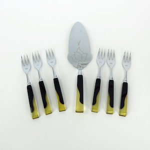 Peut inclure: Un ensemble de fourchettes en acier inoxydable et une pelle à gâteau. Les fourchettes ont des manches noirs et jaunes. La pelle à gâteau présente un motif floral et une poignée noire. L'ensemble est disposé sur une surface blanche.