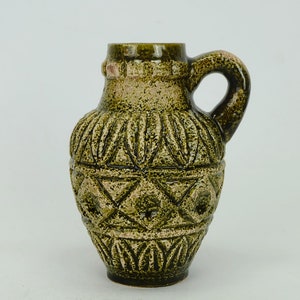 May include: A green ceramic vase with a geometric pattern. The vase has a handle and a rounded body.
