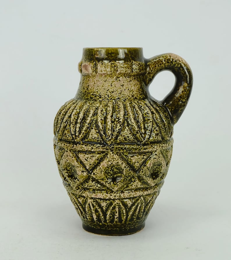 May include: A green ceramic vase with a geometric pattern. The vase has a handle and a rounded body.