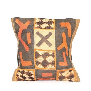 Puede incluir: Una almohada cuadrada con fondo negro y un patrón geométrico en naranja y marrón. El patrón está formado por cuadrados y diamantes.