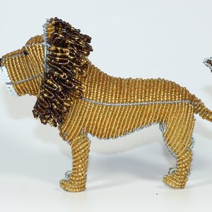 May include: A beaded lion figurine with a golden body and a brown mane. The lion is standing on all four legs with its tail curled up.