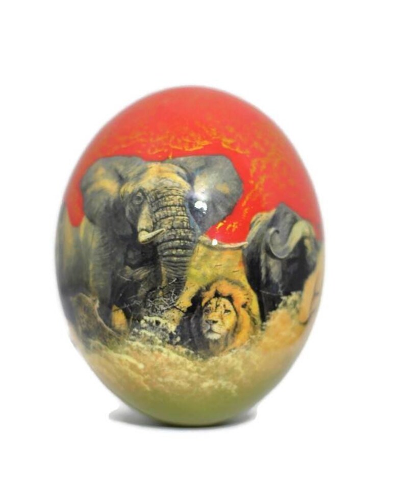 May include: A hand-painted, spherical, decorative egg with a red, orange, and green background. The egg features a detailed illustration of an elephant, a lion, and a rhinoceros in a savanna setting.