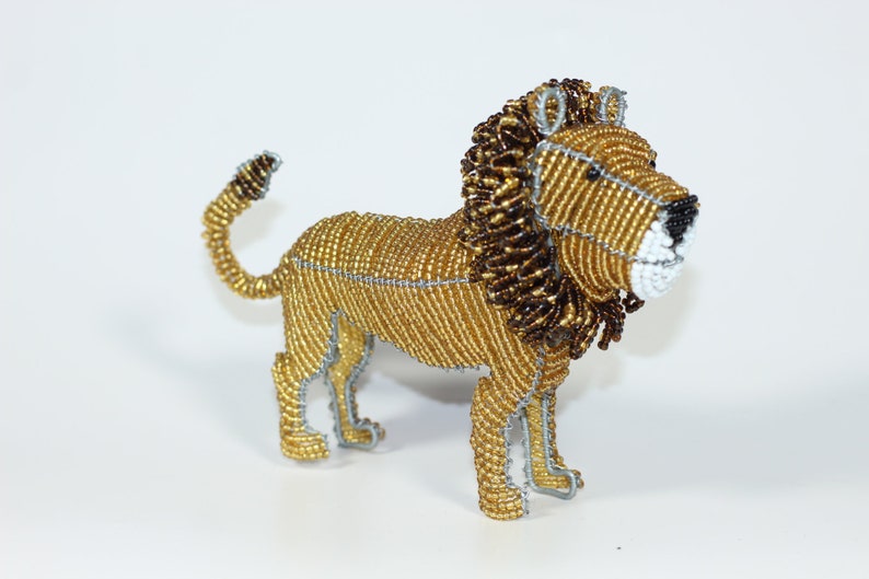 May include: A beaded lion figurine with a gold and brown mane. The lion is standing on all four legs and has a long tail.