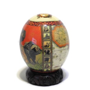 May include: A decorative ostrich egg with a map of Africa and images of African animals, including a lion, rhino, elephant, and buffalo. The egg is on a dark wood stand.