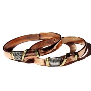 May include: Two copper bracelets with a silver and copper wire design. The bracelets are stacked on top of each other.