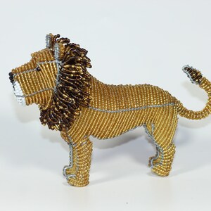 May include: A beaded lion figurine with a gold body, brown mane, and silver wire accents. The lion is standing on all four legs with its tail curled up.
