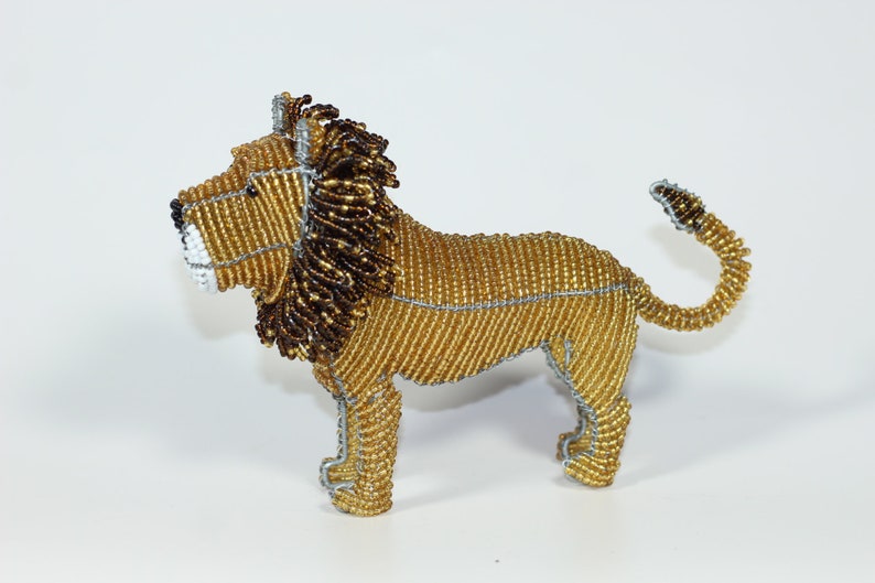 May include: A beaded lion figurine with a gold body, brown mane, and silver wire accents. The lion is standing on all four legs with its tail curled up.