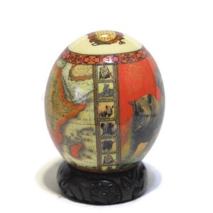 May include: A decorative globe egg with a map of Africa and images of animals, including a rhinoceros, lion, and elephant. The egg is on a dark wood stand.