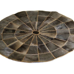Puede incluir: Una alfombra redonda de piel de vaca gris y marrón con un patrón circular de formas geométricas.