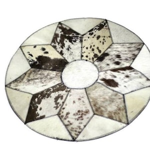 May include: A round, white and black cowhide rug with a starburst pattern. The rug is made of several pieces of cowhide sewn together.