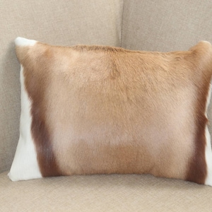May include: A rectangular throw pillow featuring a tri-color cowhide pattern. The center panel is a light tan, flanked by two vertical bands of dark brown, and finished with white edges on the far left and right sides of the pillow cover.