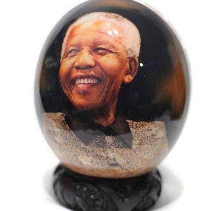 Puede incluir: Una foto en blanco y negro de Nelson Mandela está impresa en un orbe de vidrio redondo. El orbe está sentado sobre una base de madera oscura con tallas intrincadas.