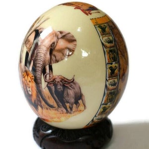 Cáscara de decoupage de los Cinco Grandes de África. Huevo de avestruz con los Cinco Grandes Animales y mapa africano con flores de protea sobre un fondo transparente. Envío exprés