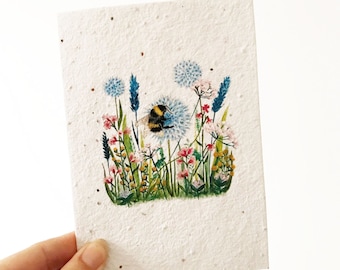 Peut inclure: Une carte blanche avec une illustration aquarelle d'un bourdon sur une fleur de pissenlit entourée d'autres fleurs et de verdure.