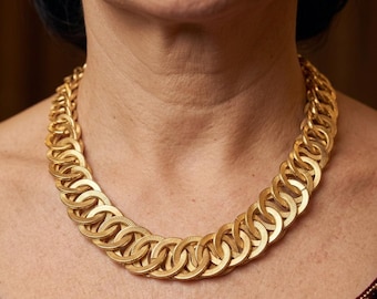 Puede incluir: Un collar dorado con un diseño repetitivo de círculos entrelazados. El collar es de metal y tiene una superficie texturizada. El collar se lleva alrededor del cuello.