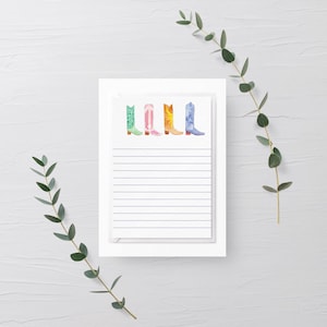 May include: A white notepad with a lined page and a row of five colorful cowboy boots at the top. The boots are green, pink, orange, blue, and purple.