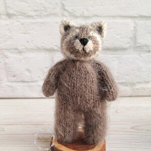 Peut inclure: Un petit jouet en peluche en tricot marron en forme de raton laveur. Le jouet est debout sur une tranche de bois.