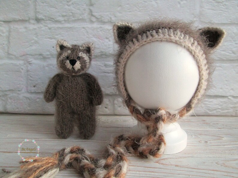 Peut inclure: Un bonnet en tricot marron en forme de raton laveur avec des oreilles duveteuses et une bordure blanche en crochet. Le bonnet est sur une t&ecirc;te de mannequin blanche et a une queue en laine marron et blanche.