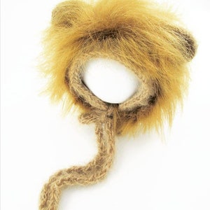 Puede incluir: Un gorro de punto marr&oacute;n en forma de le&oacute;n con una cola larga. El gorro tiene una melena y orejas peludas.