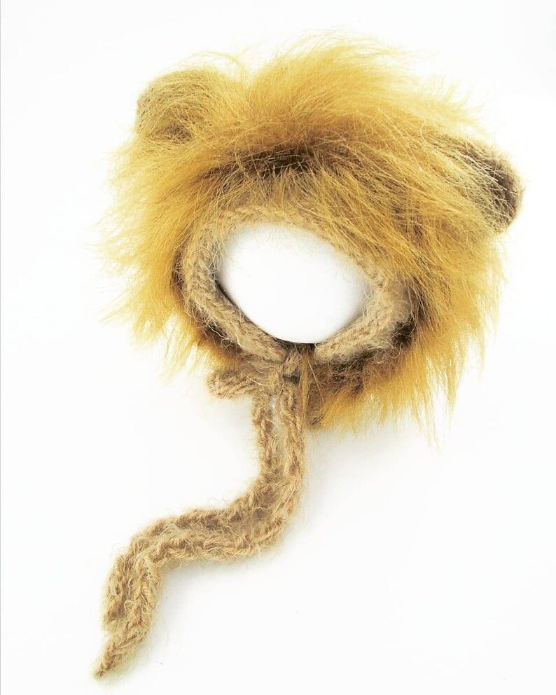 Puede incluir: Un gorro de punto marr&oacute;n en forma de le&oacute;n con una cola larga. El gorro tiene una melena y orejas peludas.