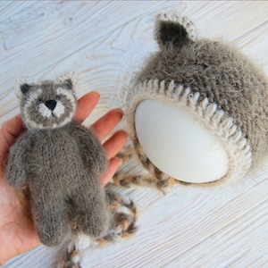 Peut inclure: Un bonnet en tricot marron et blanc avec des oreilles en fourrure et un jouet en peluche marron et blanc assorti. Le bonnet est sur une surface blanche.