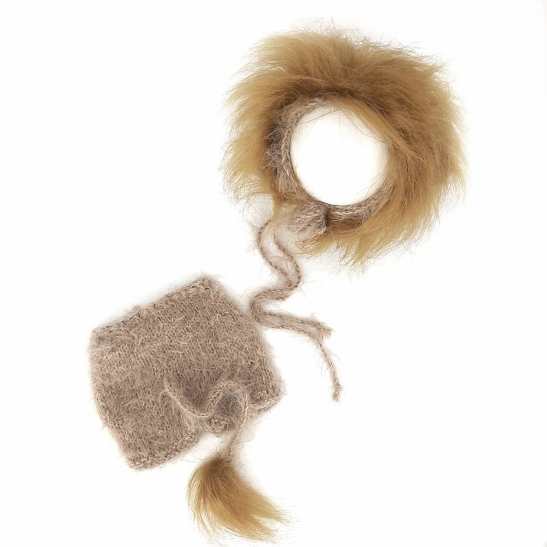 May include: A brown knitted baby hat with a matching headband. The headband is made of faux fur and has a fluffy texture. The hat has a tie at the bottom and a fluffy tail.