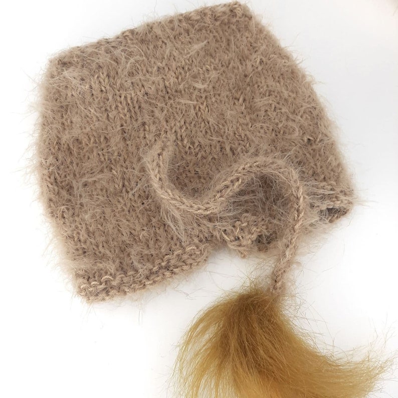 May include: A brown knitted hat with a long, fluffy tail. The hat is made of a soft, fuzzy yarn and has a simple, classic design.