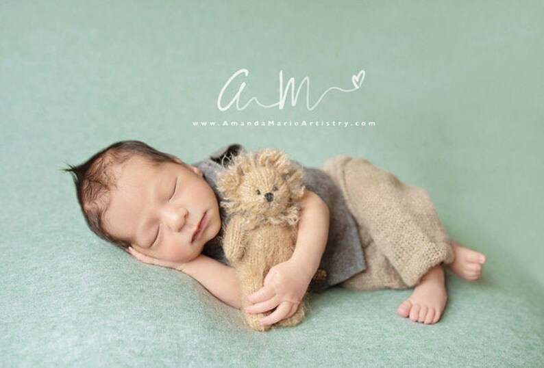 Puede incluir: Un beb&eacute; reci&eacute;n nacido duerme sobre una manta verde claro, sosteniendo un oso de peluche de punto marr&oacute;n. El beb&eacute; lleva una camisa gris y pantalones marrones.
