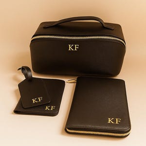 May include: A black travel set comprising a cosmetic bag, wallet, and luggage tag. Each item features a gold zip and the initials "KF" in gold. The cosmetic bag has a handle.