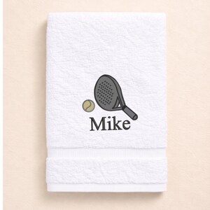 May include: White towel with an embroidered tennis racket and ball design. The racket is gray, the ball is yellow, and the name "Mike" is embroidered in black. The towel is made of a soft, absorbent material.