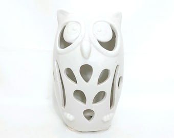 May include: A white ceramic owl figurine with cut-out designs. The owl has large, round eyes and a beak. The body features leaf-shaped cutouts. The figurine is a decorative item, likely for home decor.