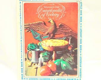 May include: Vintage cookbook titled "Woman's Day Encyclopedia of Cookery, Vol. 1." The cover features an eagle, a pie, and various food items. The book's title is in a decorative font, with additional text around the border.