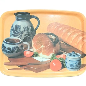 May include: A rectangular serving tray with a printed image of a still life. The image includes a loaf of bread, a ham, tomatoes, a mug, a pitcher, and a small jar. The tray has a yellow border.