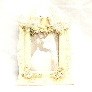 May include: Cream-colored picture frame with a wedding theme. The frame features two doves at the top, a floral arrangement, and rose accents. The frame holds a black and white photo of a couple.