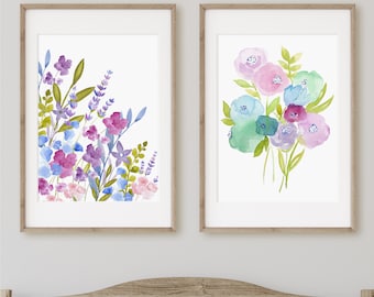 May include: Two framed watercolor paintings of floral bouquets. The first painting features a cluster of purple, pink, and blue flowers with green leaves. The second painting features a bouquet of pink, blue, and green flowers.