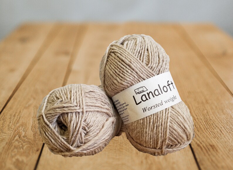 Puede incluir: Dos ovillos de lana beige de peso grueso, uno con una etiqueta que dice "Lanaloft Worsted weight".