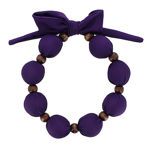 May include: A purple fabric necklace with a bow at the top and wooden beads. The necklace is made of a series of round, fabric-covered beads.