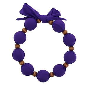 May include: A purple fabric necklace with wooden beads. The necklace is tied with a bow at the top.
