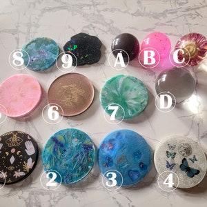 Puede incluir: Diez posavasos redondos de resina con varios diseños. Los posavasos presentan una variedad de colores, incluyendo rosa, azul, verde, negro y blanco. Algunos posavasos tienen diseños abstractos, mientras que otros tienen diseños más detallados, como mariposas, medusas y cuerpos celestes.