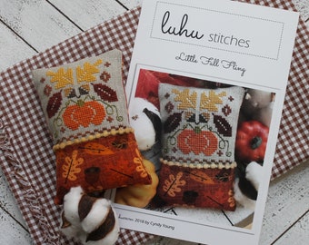 Könnte beinhalten: Ein Kreuzstichmuster für ein kleines Kissen mit einem Kürbis und Herbstblättern. Das Muster heißt "Little Fall Fling" und ist von Luhu Stitches. Das Muster ist auf weißem Hintergrund mit braunem Text.